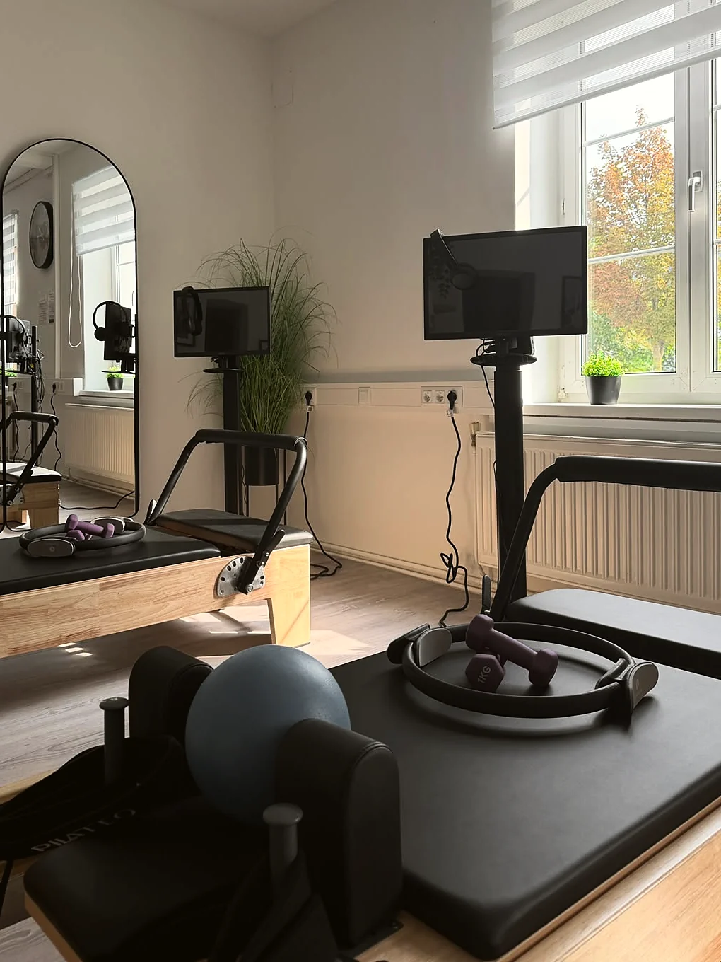 Reformer mit eigenem Monitor am Fenster, dahinter ein zweiter Platz und die bogenförmigen Spiegel.